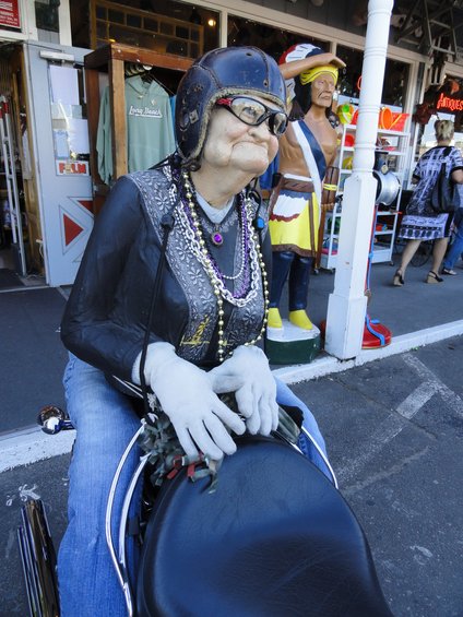 Mannequin dressed as an old woman wearing a helmet and jewelry, sitting on a motorcycle