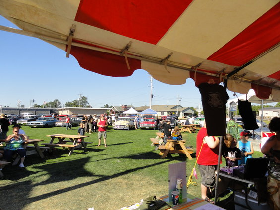 Outdoor car show scene with classic cars and people gathered under a tent