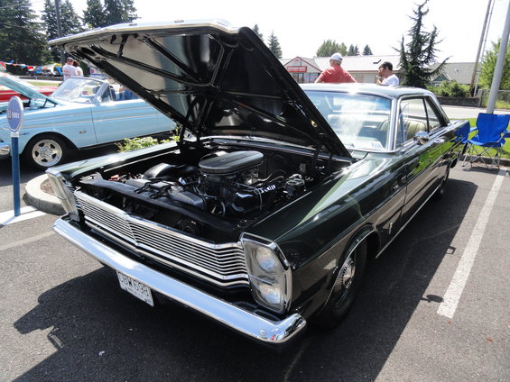 dark green coupe, hood open showing engine, parked next to a light blue convertible