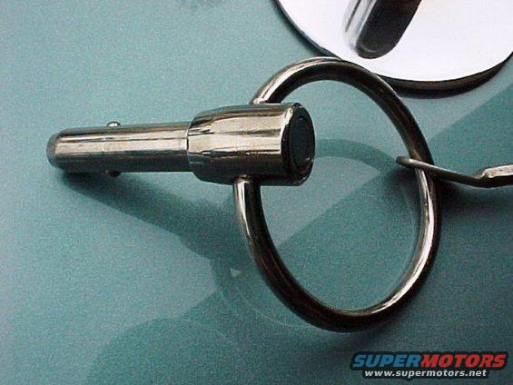 Close-up of a chrome hood pin with a large ring attached, resting on a teal surface
