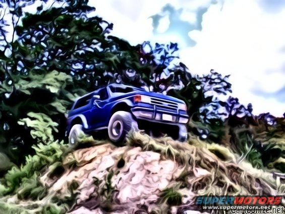 Blue SUV climbing a dirt hill with trees and sky in background. Supermotors.net logo visible