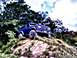 1992 Ford Bronco - A blue SUV navigates a steep, rocky incline under a cloudy sky.