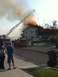 2006 Ford E350 - Emergency responders work to extinguish a house fire, with a ladder truck directing water onto the flames.