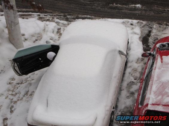 Car covered in snow with driver's door open, parked next to a red car