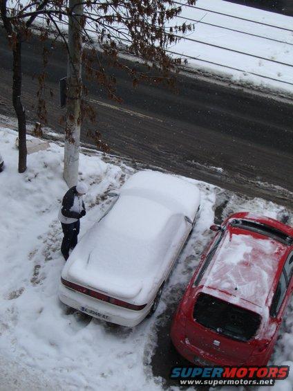 White car covered in snow, rear view. A person stands nearby