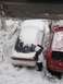 1995 Ford Probe - A person clears snow from the rear window of a white car parked next to a red car in a snowy environment.