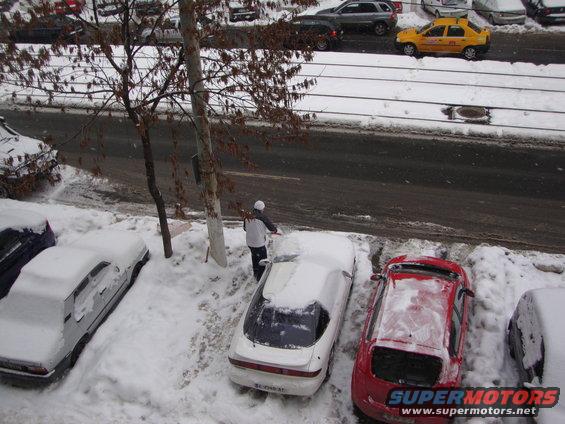 Several cars covered in snow, with a person shoveling snow from one