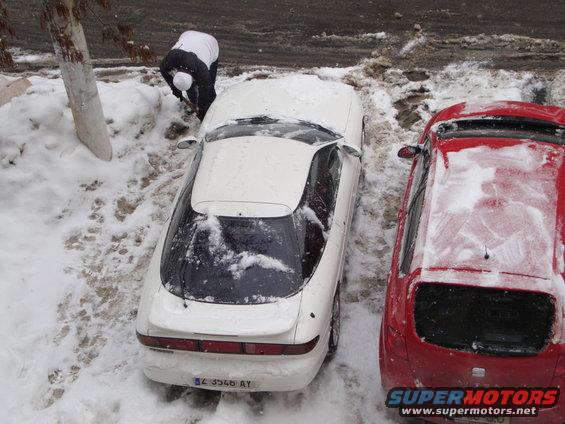 White coupe with a sloping rear window and a full-width taillight bar, parked in snow