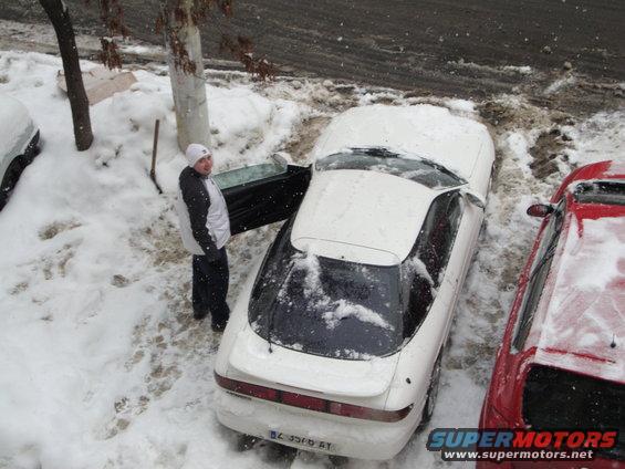 White coupe with door open in snow, parked next to a red car