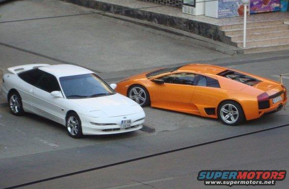 White Ford Probe parked next to an orange Lamborghini. License plate visible on Probe