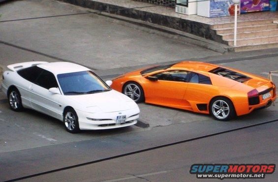 White 1995 Ford Probe parked next to an orange Lamborghini, front 3/4 view