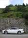 1995 Ford Probe - A white 1995 Ford Probe is parked on the side of a road, with a stone wall and a lush green hill in the background.