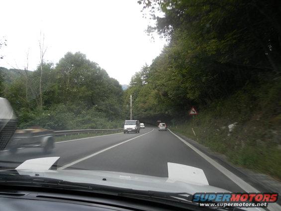 View from car dashboard looking at a winding road with trees and other vehicles