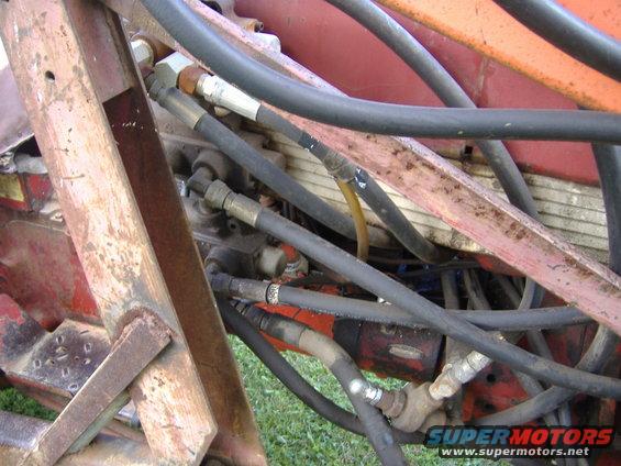 Close-up of hydraulic hoses and rusty metal frame, with "SUPERMOTORS" text at bottom right