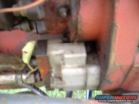Close-up of a hydraulic pump assembly with a light-colored reservoir, attached to red machinery