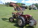 1988 Ford Bronco - A red tractor with a front loader attachment sits in a grassy field next to farm buildings.