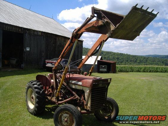 Red tractor with front loader attachment parked on grass in front of a barn