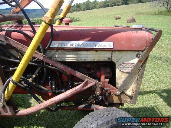 Red and white International 240 tractor with yellow hydraulic arms, close-up on the side