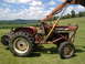 1988 Ford Bronco - A red tractor with a front loader attachment is parked in a grassy field with a cornfield and rolling hills in the background.