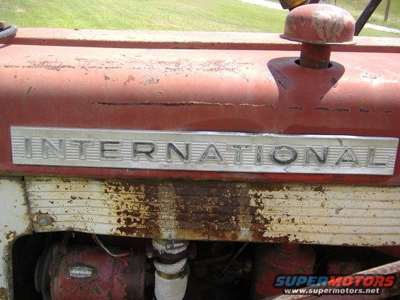Close-up of 'INTERNATIONAL' badge on a red tractor hood with rust