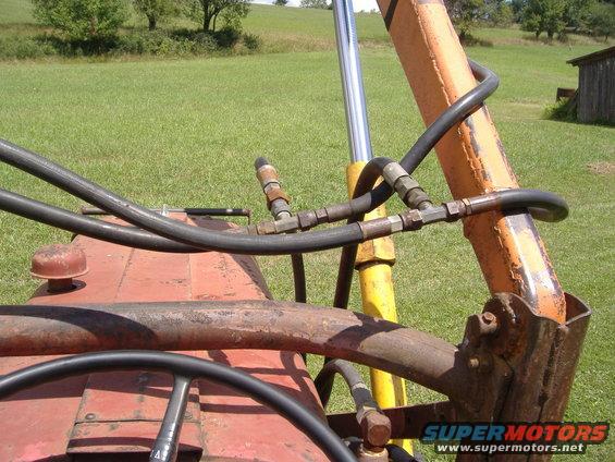 Close-up of hydraulic hoses and cylinders on a red tractor with a loader arm