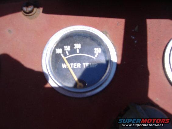 Water temperature gauge with needle pointing to 100 degrees, set in a dark red dashboard
