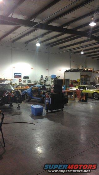 Workshop with a blue car being worked on, a yellow car in the background, and another car on a lift