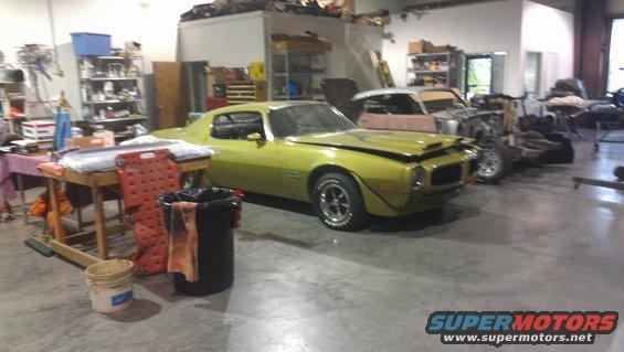 Yellow 1973 Chevrolet Camaro coupe with hood open, parked in a cluttered garage