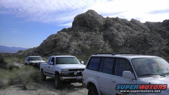 three white off-road vehicles parked on a dirt trail in a desert landscape with rocky mountains in the background