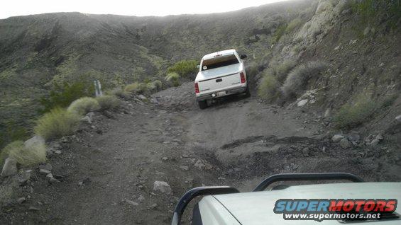 White pickup truck driving on a steep, rocky desert trail