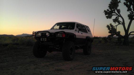 White and black off-road SUV with large tires parked in desert at sunset