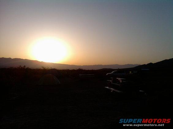 Truck parked at campsite with tent and mountains at sunset
