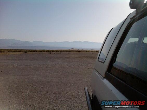 Silver SUV side view with a cap, parked in a dry, barren landscape with mountains in the distance