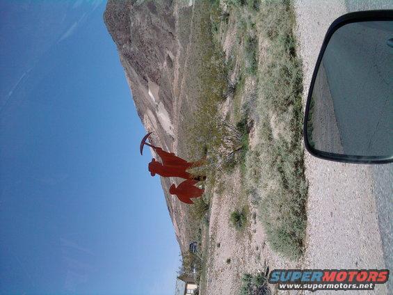 Desert landscape with a miner sculpture, seen from a vehicle's side mirror