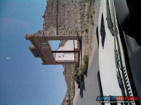 White vehicle parked next to a ruined stone building with a blue sign