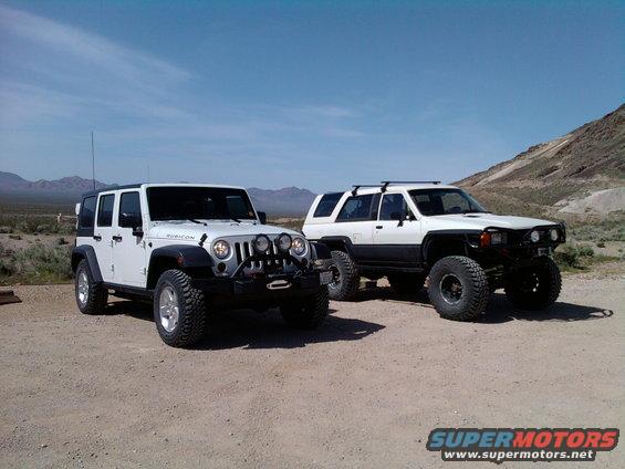 White Jeep Wrangler Rubicon and white Toyota 4Runner parked on dirt road in desert landscape
