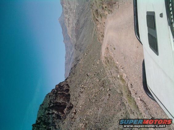 White vehicle on a dirt road next to a steep mountain drop-off