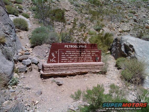 Petroglyph sign with text about Indian rock carvings, set in a rocky desert area