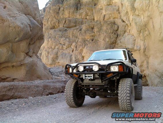 White SUV with off-road modifications parked on a dirt road in a rocky canyon