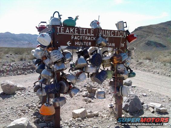 Teakettle Junction signpost covered in hanging kettles in a desert landscape