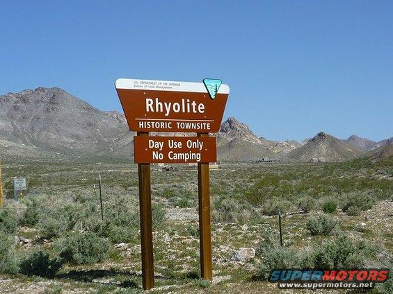 Brown sign for Rhyolite Historic Townsite with text 'Day Use Only. No Camping.' in a desert landscape