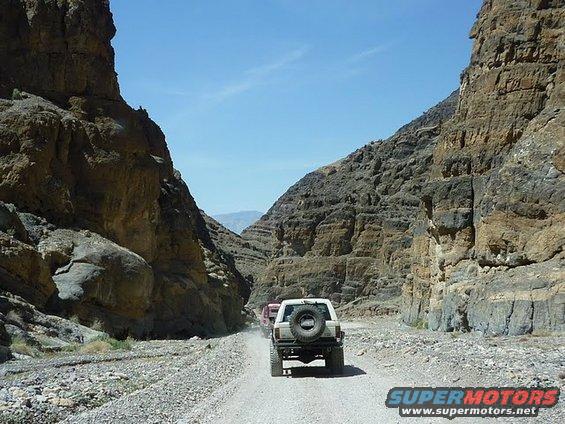 1985 Toyota 4Runner and other SUVs driving on a dirt road in a rocky canyon