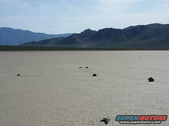 rocks leaving trails on dry lake bed with mountains in background
