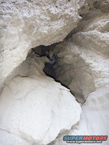 Rock formation with a dark opening in the center, showing a Supermotors logo at the bottom right