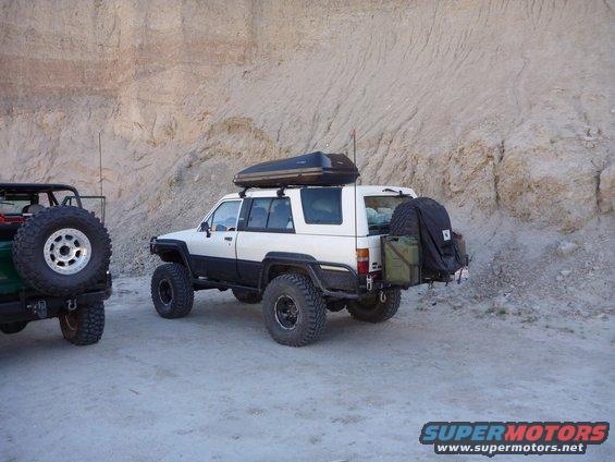 1985 Toyota 4Runner with roof box and rear storage, parked next to a green Jeep with a spare tire mounted on the back