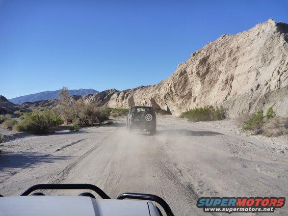 Dark green SUV with a spare tire on the back drives on a dusty desert road