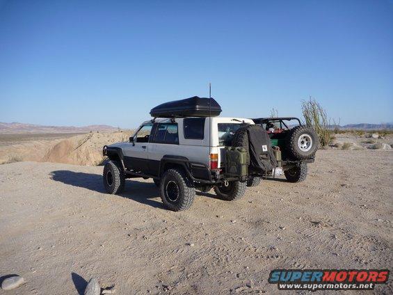 1985 Toyota 4Runner with roof box and jerry cans, parked in desert next to another off-road vehicle