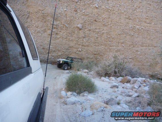 Green off-road vehicle with a white top and black roll cage parked on a dirt road