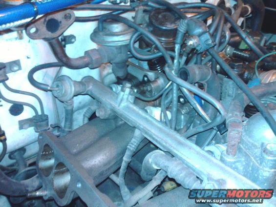 Engine bay with hoses, wires, and metal components. Visible text: SUPERMOTORS www.supermotors.net