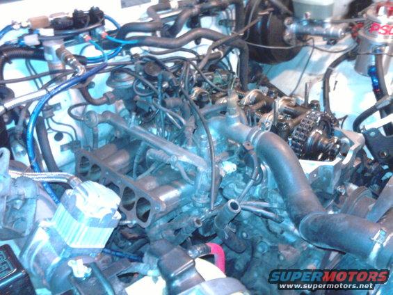 Engine bay with exposed engine components, hoses, and wiring. Visible text: SUPERMOTORS